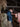 Person wearing a cowboy hat and blue jacket standing next to a stack of hay in a barn.