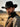 Model wearing black Western hat with leather band and gold studs, minimal modern cowboy aesthetic.