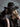 Black felt western hat with studded band and leather vest against gray background.