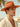 Man wearing orange wool felt Western hat with green velvet band, sunlit beach background.